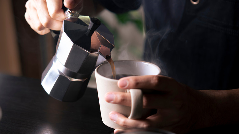 Hands pouring coffee from moka pot into white cup