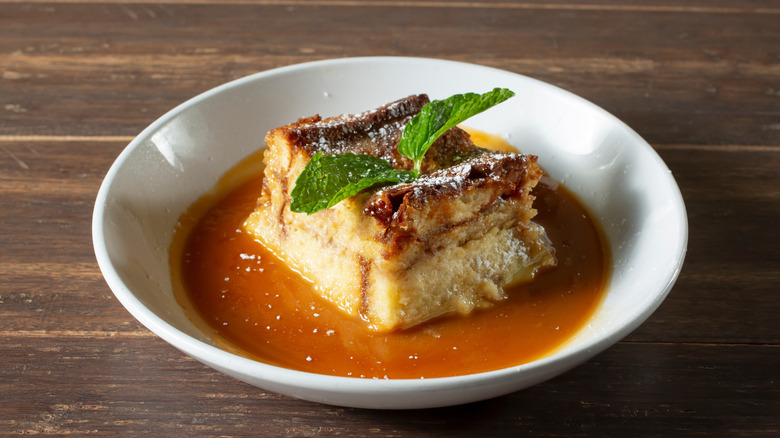 A slice of bread pudding drenched in sauce topped with a mint leaf