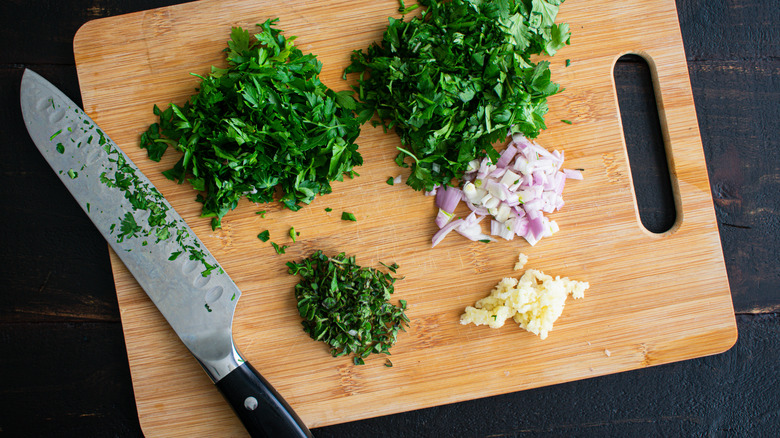 A chef's knife with herbs on a cutting board