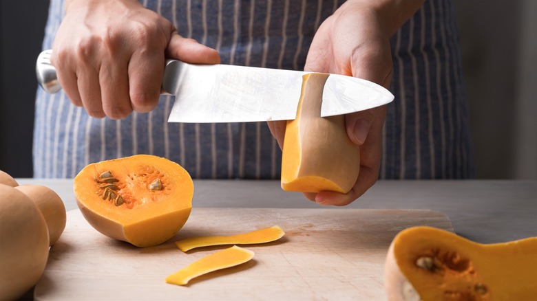 Hands peeling half of butternut squash