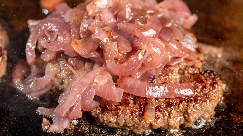 caramelized onions on cooking hamburger on grill