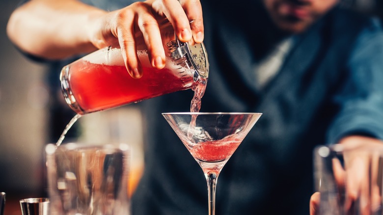 A bartender pouring a Cosmopolitan from a shaker into a martini glass
