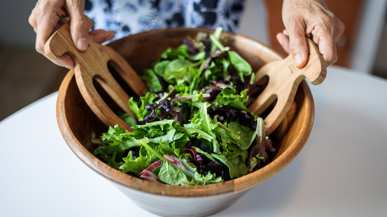 tossing various salad greens in a wooden bowl