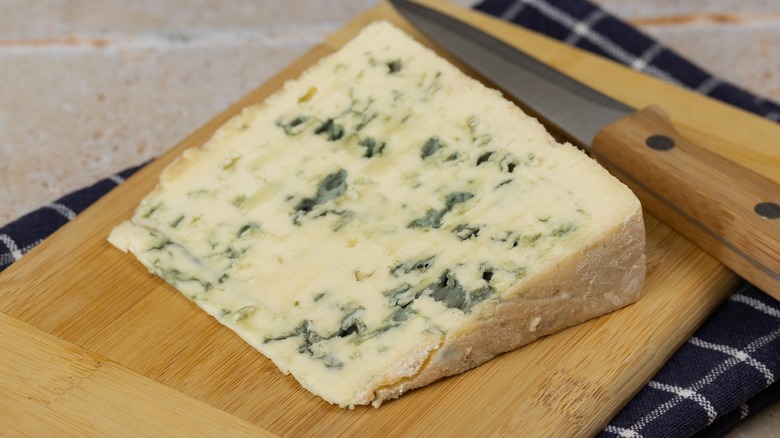 A slice of Roquefort blue cheese on a cutting board