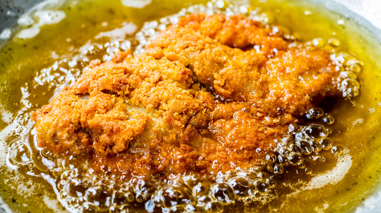 Pork katsu frying in pan in a pool of oil.