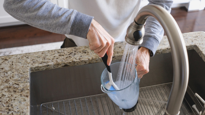 Man cleaning a blender in the sink with a scrub brush.