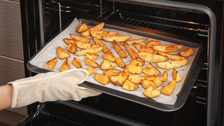 Hand placing baking sheet of fries in oven