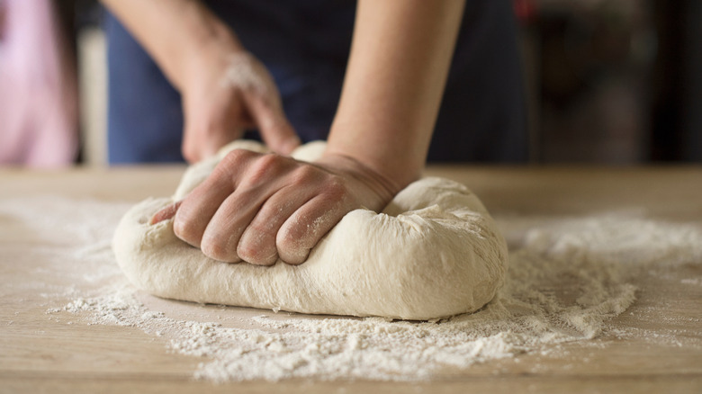 Two hands kneading dough on a floured board