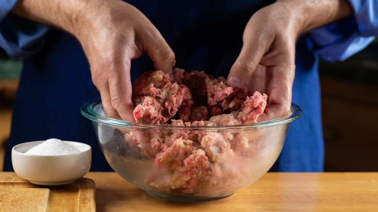 Hands mixing ground beef in a glass bowl