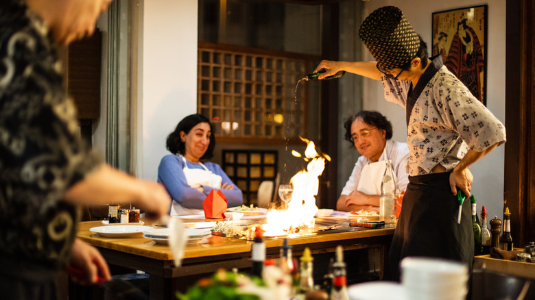 A couple watching in amusement as chef cooks food with high flame at their table