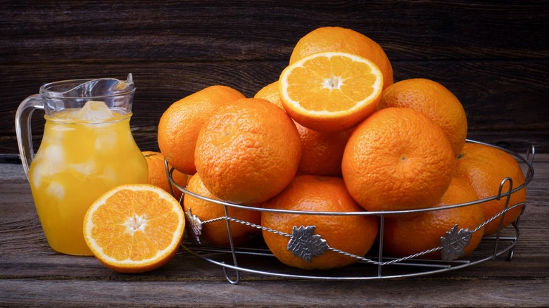 A dish of Valencia oranges next to a pitcher of orange juice