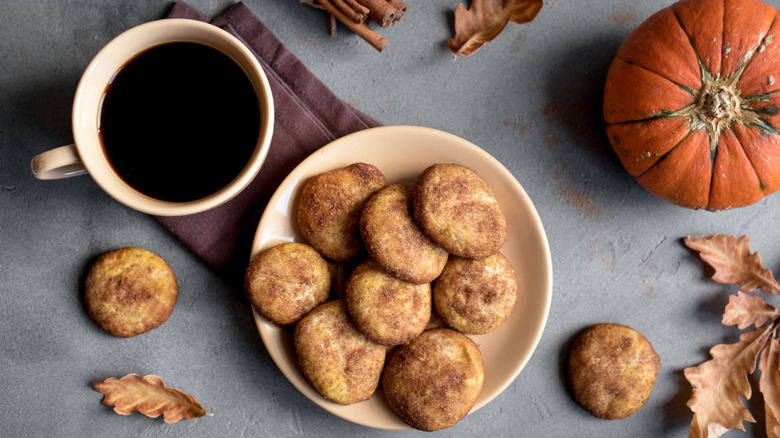 Plate of snickerdoodle cookies between pumpkin and mug of coffee on grey table