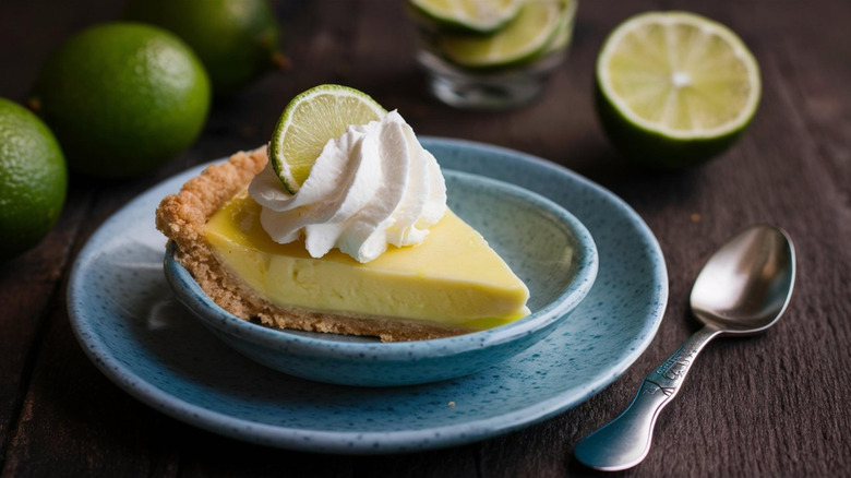 Blue plate with slice of key lime pie surrounded by fresh limes on wooden table