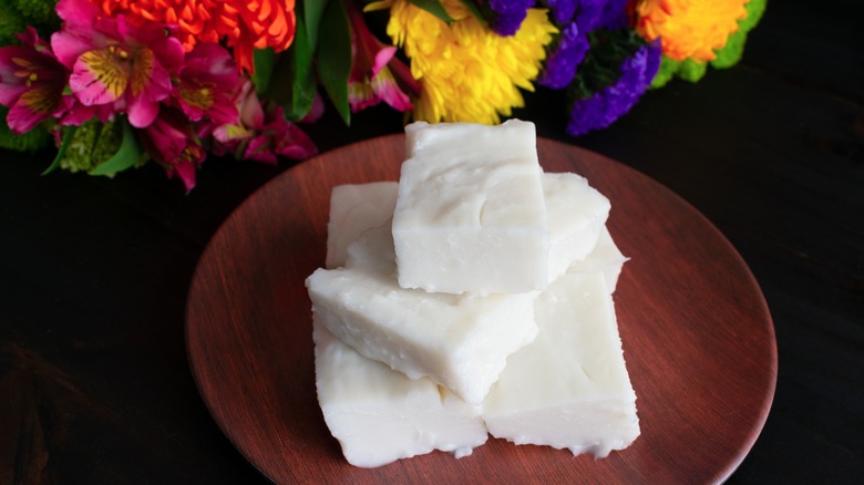 Haupia squares on wooden plate in front of colorful flowers