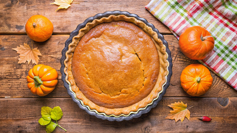 Overhead shot of pumpkin pie on wooden table surrounded by small pumpkins and leaves