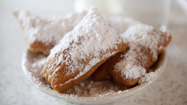 White plate filled with beignets coated in a thick layer of powdered sugar