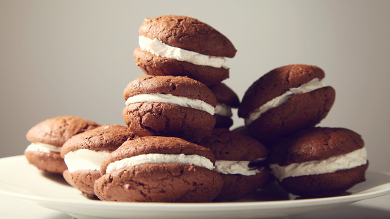 Stack of chocolate whoopie pies on white a plate with a pale reddish background