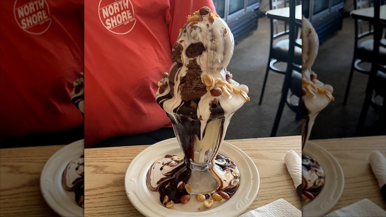 Tin roof sundae on white plate standing on a table in a diner with a customer sitting in the back