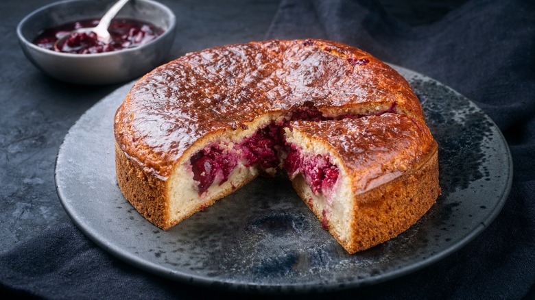 Gateau basque assembled on a dark plate sitting on a black counter with a slice taken out and a bowl of fruit in the back