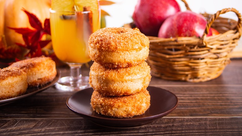 Wooden table with stack of apple cider donuts, apple drink and basket of apples