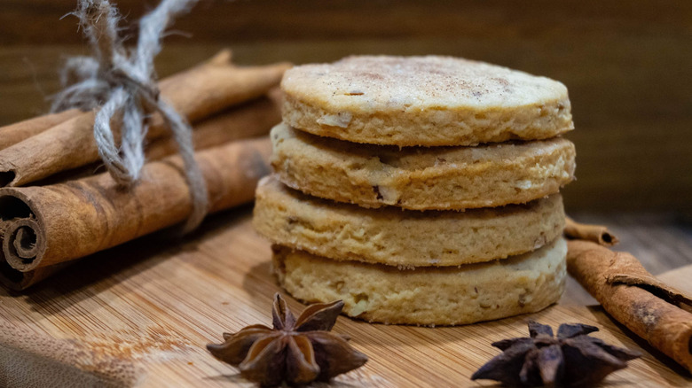 Stack of biscochitos next to cinnamon stick and star anise on wooden table