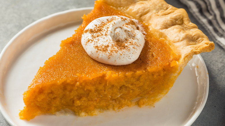 Slice of sweet potato pie with whipped cream on white plate