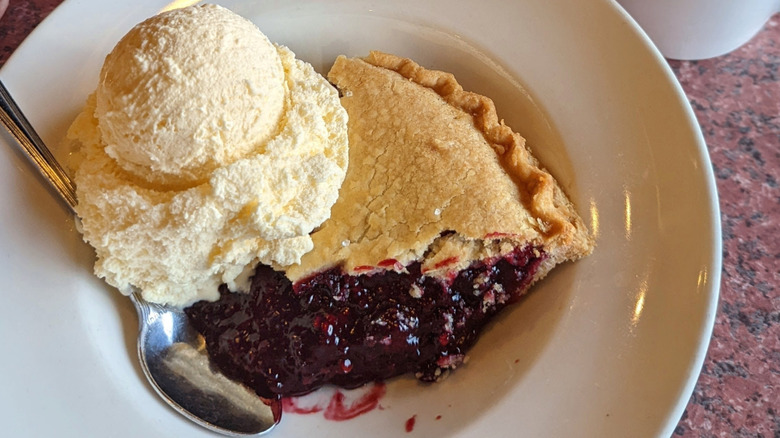 Slice of marionberry pie and ice cream on white plate sitting on a red marble counter