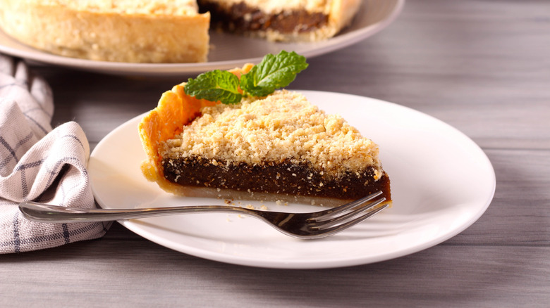 White plate with slice of shoofly pie on wooden table with the whole pie in the back