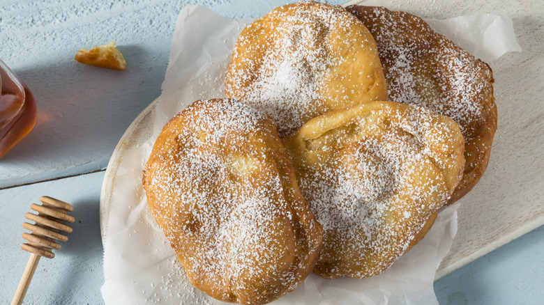 White cloth basket packed with doughboys on blue table with honey on the side and a wooden tool