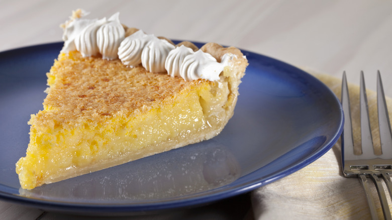 Slice of chess pie with whipped cream on a blue plate with a fork on the side