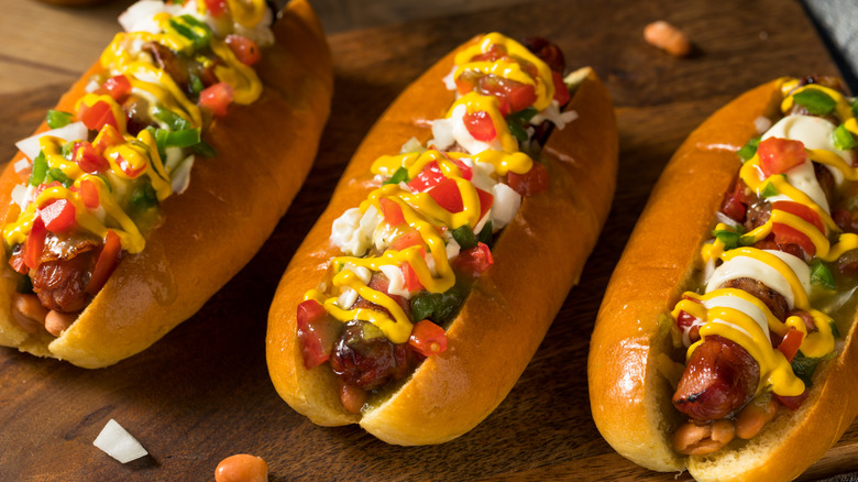 Three Sonoran hot dogs with colorful toppings on wood board