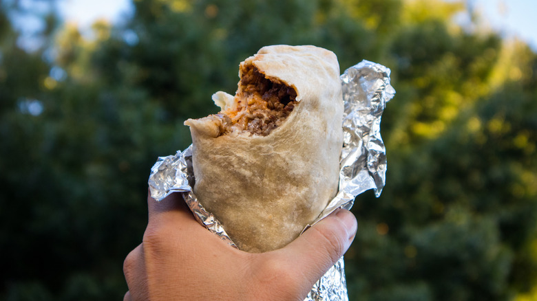 Hand holding a burrito partially wrapped in foil with bite taken out of it