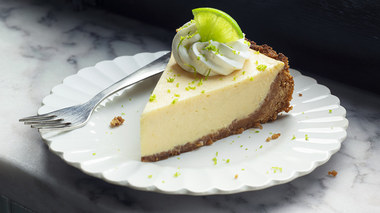 Slice of key lime pie and fork on white plate on grey marble table