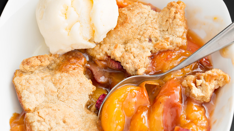 Close-up of peach cobbler in white bowl with scoop of ice cream