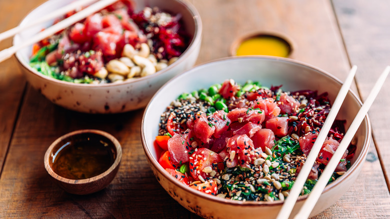 Two colorful poke bowls on wooden table with ramekins