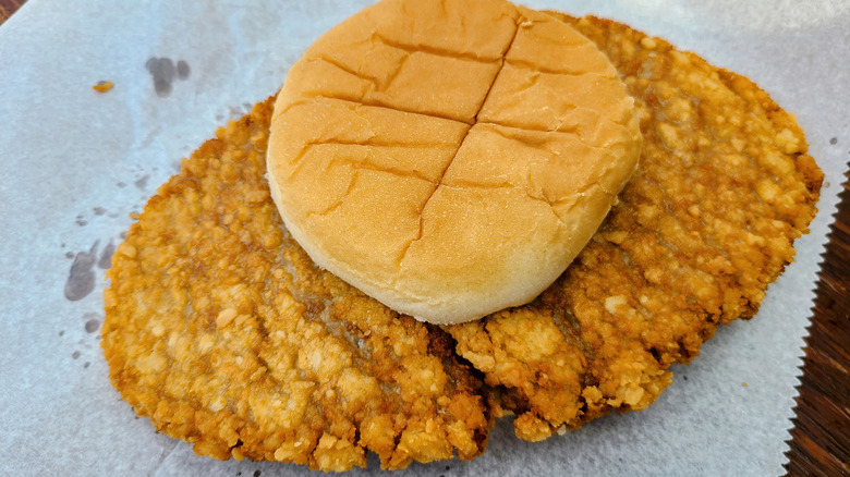 Large fried pork tenderloin sandwich with small bun on wax paper