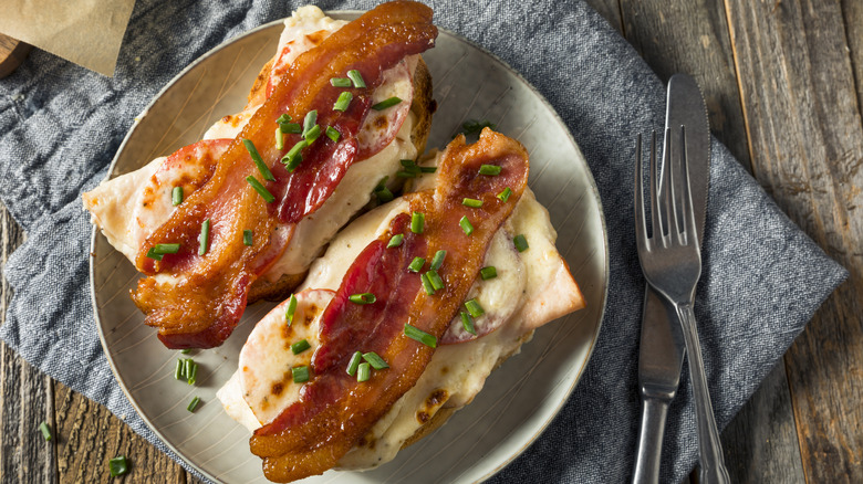 Open-faced Hot Brown sandwich with tomato, cheese, and bacon and green onion garnish