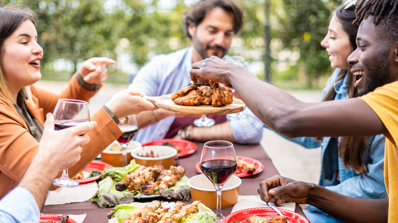 Group of friends eating meat at table outside