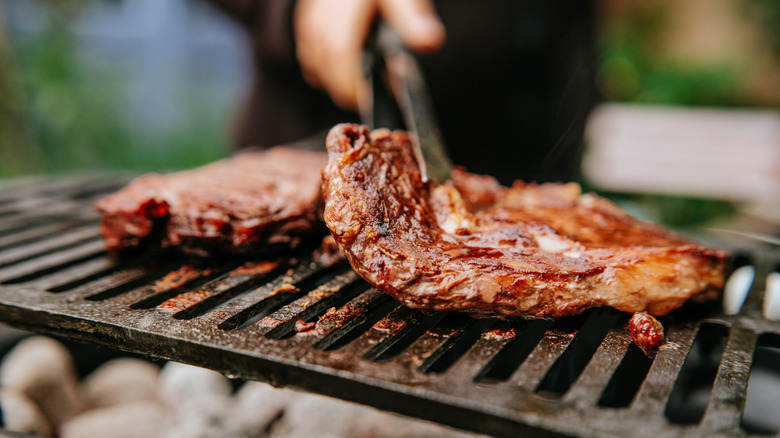 Hand tending to barbeque steaks on outdoor grill