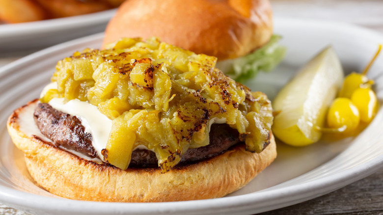 Open-face cheeseburger with pile of grilled green chiles on white plate