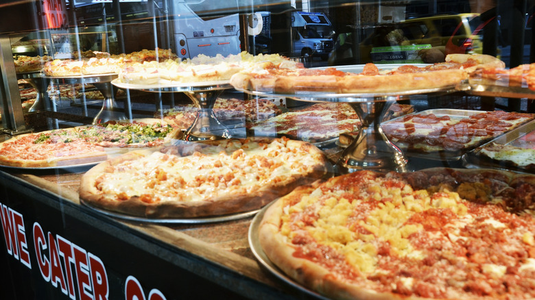 New York-style pizza pies behind glass case at pizzeria in NYC