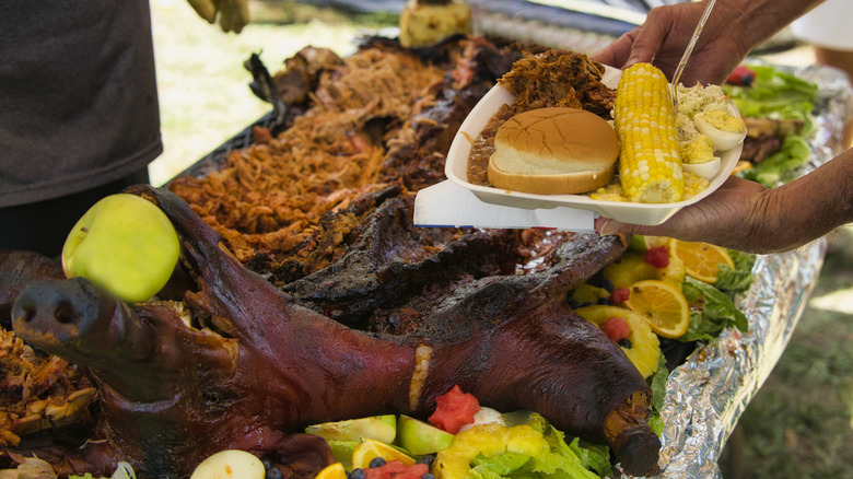 People putting pork on plates from roasted whole hog