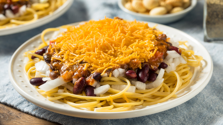 Chili, onions, and shredded cheese over spaghetti noodles on plate