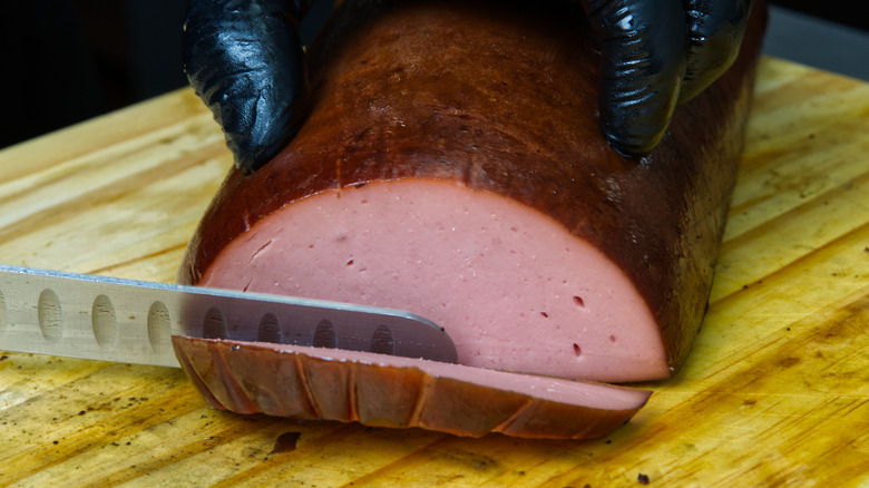 Close-up of hand slicing smoked bologna on cutting board