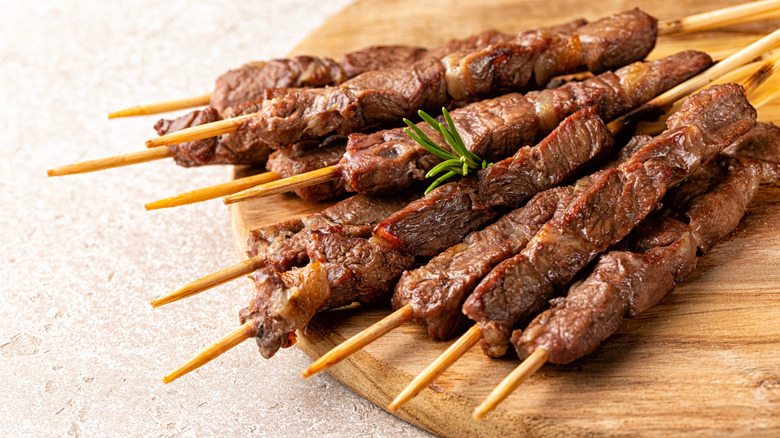 Lamb skewers on wood board with sprig of rosemary