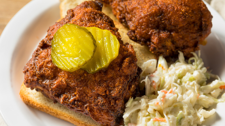 Close-up of hot chicken on bread with pickles and side of coleslaw