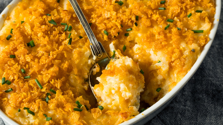 Close-up of spoon scooping cheesy potato casserole with crushed corn flakes