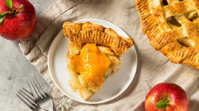 Slice of apple pie on white plate with melted cheddar on top