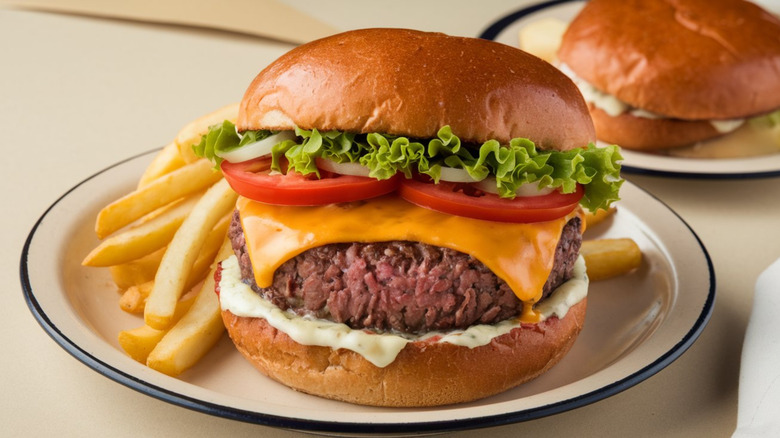 Bison burger with cheese, lettuce, tomato, with fries on off-white background