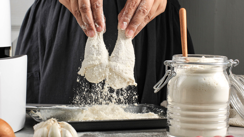 Hands coating fried chicken 